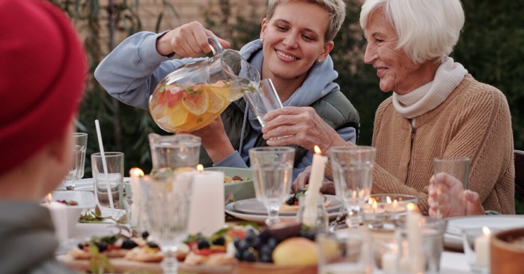 Positive lady pouring drink into glass for elderly woman while having dinner with family on terrace